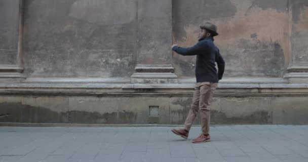 Κομψό αφροαμερικάνικο αρσενικό άτομο που χορεύει και κάνει κύκλους περπατώντας κατά μήκος της παλιάς πόλης. Χαρούμενος γενειοφόρος που κινείται με ρυθμό. Έννοια των θετικών συναισθημάτων. Εξωτερικές πόρτες. — Αρχείο Βίντεο