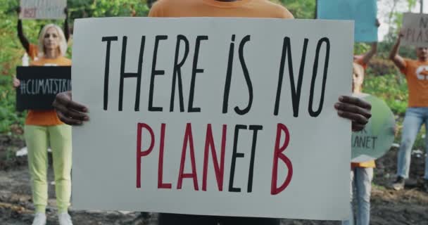 Crop view of afro american person holding carton placard with there is no planet b writing. Militant debout dans un groupe de personnes dans du bois plein de déchets. Concept de destruction de la nature. — Video