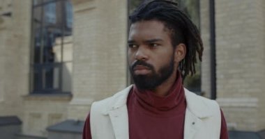 Şehir caddesinde dikilen sakallı, ciddi bir gencin bakışını yakından izleyin. Balıkçı yaka kazaklı, açık havada poz veren yakışıklı Afroamerikalı adamın portresi..