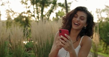 Komik bir mesaj alırken gülüp, akıllı telefon kullanan çekici bir kadın. Şehir parkında otururken yazı yazan ve dokunan neşeli bir kadın. Pozitif duyguları kavra.
