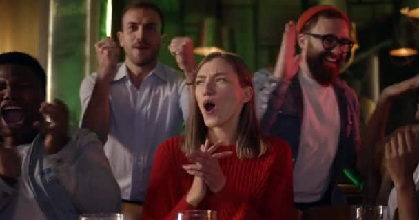 Grupo de amigos alegres batendo palmas e dando mais cinco depois de cantar hino nacional no pub. Pessoas multiétnicas se reúnem para assistir a jogos esportivos e olhar para a tela da TV. — Vídeo de Stock