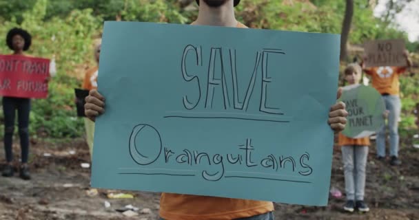Vista da colheita da pessoa masculina segurando cartaz de papelão com salvar orangotangos escrita. Ativista de pé em grupo de pessoas na floresta cheia de lixo. Conceito de protecção dos animais. — Vídeo de Stock