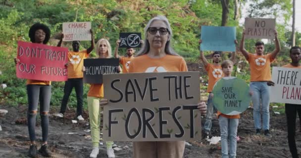 Ώριμη γυναίκα κρατώντας πλακάτ με σώσει το γράψιμο του δάσους, ενώ στέκεται μπροστά από οικολόγοι ακτιβιστές. Ομάδα ανθρώπων με πανό και συνθήματα που κοιτάζουν την κάμερα στο πάρκο γεμάτη σκουπίδια. — Αρχείο Βίντεο