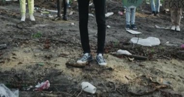 Pankartlı Afrikalı adamın en alttan en üstte görüntüsü aktivist grubun önünde duran bir gezegen b yok. Sancakları ve sloganları olan çeşitli insanlar çöplerle dolu parkta kameraya bakıyorlar..