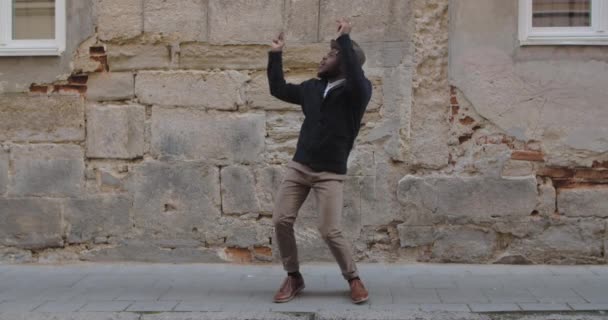 Fröhliche männliche Person, die tanzt und singt, während sie an der Stadtstraße steht. Millennial afroamerikanischer Mann mit Bart in stylischer Kleidung, der Musik hört und sich in Reimen bewegt. Konzept des Spaßes. — Stockvideo