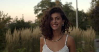Açık havada yürürken dalgalı saçlı, gülümseyen neşeli esmer kadını yakından çek. Kameraya poz veren ve bakan oyuncu Latin kadın portresi. Yaz mevsimi kavramı.