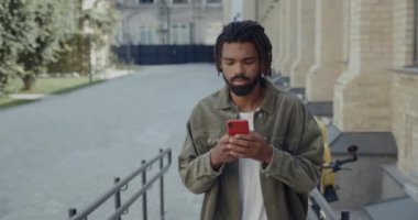 Şehirli caddede yürürken internette gezinen rastalı ırklı genç bir adam. Akıllı telefon iletişim kavramını kullanarak daktilo eden ve gülümseyen sakallı genç adam..