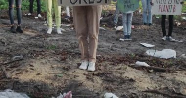 Tepeden tırnağa pankartlı bir kadın, çevreci aktivistler grubunun önünde ormanı kurtarıyor. Sancakları ve sloganları olan çeşitli insanlar çöplerle dolu parkta kameraya bakıyorlar..