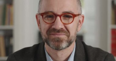 Kameraya bakıp gülümseyen takım elbiseli neşeli bir adamın portresi. Kitaplarla dolu bir odada oturan yaşlı, sakallı, gözlüklü adamın yakın görüntüsü. İnsanların vesikalık fotoğrafı kavramı.