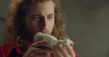 Lviv, Ukrayna - 12 Şubat 2020: yakışıklı erkek heykeltıraş ellerinde alçıdan beyaz bir ayak tutuyor ve tozunu üflüyor. Bin yıllık uzun saçlı bir adam sanat objesi yaratıyor. Sanat eseri kavramı.