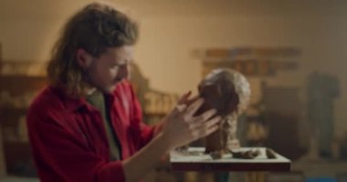 Lviv, Ukrayna - 12 Şubat 2020: Alçıdan heykel kafası yapan genç adam. Yakışıklı heykeltıraş sanatçı stüdyosunda kil büstü yaratırken yüz detaylarını ayarlıyor