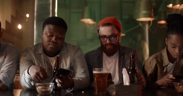 Multiethnic group of friends using their smartphones actively. Diverse people drinking beer eating snacks while being totally focused on their phones and not pay attantion to each other. — Stock Video