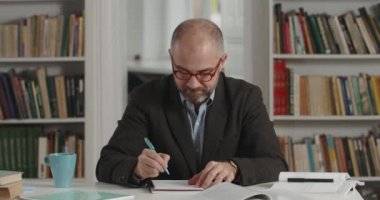 Takım elbiseli olumlu bir adamın başını kaldırıp kameraya baktığı görüntüler. Kitaplarla dolu bir odada oturmuş gülümseyen yaşlı sakallı erkek portresi. İnsanların vesikalık fotoğrafı kavramı.