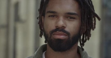 Sakallı ve bıyıklı bir adam başını çevirip kameraya bakıyor. Şehir caddesinde ayakta dikilen rastalı genç adamın portresi. Yaşam tarzı kavramı.