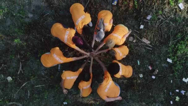 Légi felvétel a különböző aktivisták csoportjáról, akik összefogják a kezüket és tapsolnak, miközben az erdőben állnak szeméttel a földön. A csapatmunka fogalma, természetszennyezés. — Stock videók