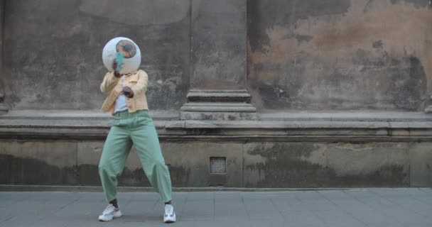 Afroamerykanin w papierowej masce na głowie tańczący na ulicy Starego Miasta. Nieznana kobieta robi zabawne ruchy trzymając smartfona. Pojęcie dobrego nastroju, zabawy. — Wideo stockowe