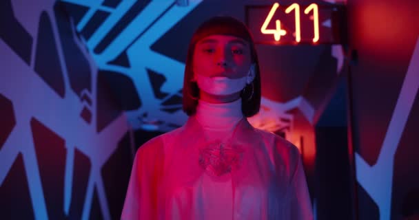 Spodní pohled na atraktivní ženu stojící na chodbě s neonovým světlem a zářícími čísly. Žena mladá osoba v futuristickém oblečení a make-up při pohledu do kamery. — Stock video