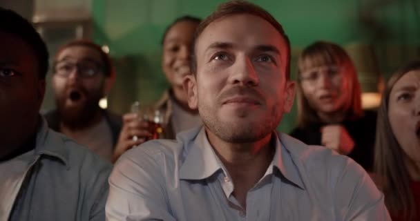 Arkadaşlarla spor izlerken bira içip gülümseyen yakışıklı adama odaklan. Barda birlikte vakit geçirirken gülen ve sevinen bir grup genç.. — Stok video