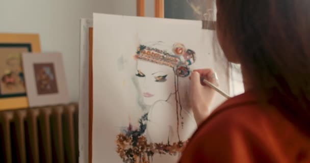 Överaxelbild av kvinnliga målare skapar vacker bild av flicka i mysig konststudio. Kvinna målning på papper med pensel och akvarell när du står framför staffliet. Zooma in. — Stockvideo