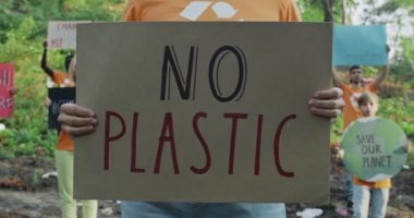 Plastiksiz karton pankart tutan kişi görüntüsü. Çöp dolu odunların içinde bir grup insanın arasında duran aktivist. Doğa tahribatı ve çevre bilinci kavramı.