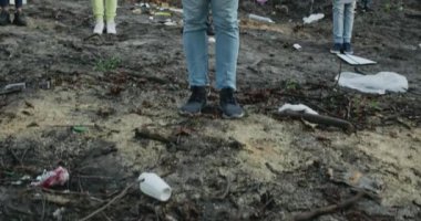 Tepeden tırnağa karton levhalı genç adam. Eylemciler grubunun önünde plastik yok. Sancakları ve sloganları olan çeşitli insanlar çöplerle dolu bir ormanda kameraya bakıyorlar..