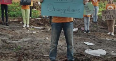 Tepeden tırnağa, başlıklı genç adam aktivist grubun önünde duran orangutanları kurtarıyor. Kartonda sloganları olan çeşitli insanlar çöplerle dolu bir ormanda kameraya bakıyorlar..