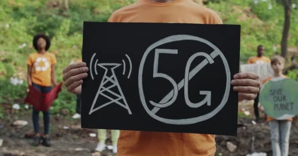 Widok upraw męskiej osoby trzymającej plakietkę kartonową bez znaku 5g. Aktywista stojący w grupie różnorodnych ludzi w drewnie pełnym śmieci. Pojęcie nieszkodliwej technologii i ekologii. — Wideo stockowe