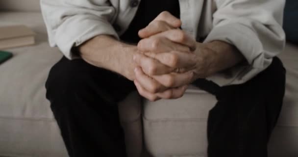 Vista de la cosecha de hombre mayor en la depresión está sentado en el sofá. Jubilado poniendo las manos juntas. Concepto de problemas de los pensionistas. — Vídeos de Stock