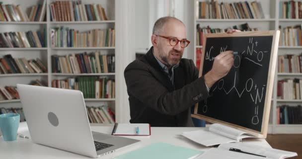 Vista de la cosecha del hombre en gafas usando tiza y pizarra mientras se explica el material. Profesor masculino enseñando en línea. Vista lateral del profesor hablando. Concepto de aprendizaje a distancia. — Vídeo de stock