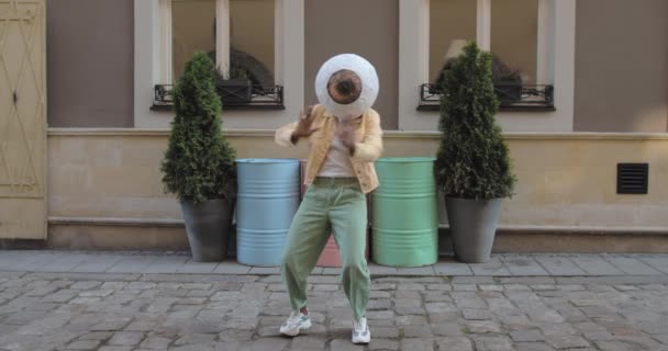 Female dancer with big eye mask on head moving in rhytm at city street. Afro american woman dancing while standing outdoors. Concept of good mood. Colourful barrels at background. — Stock Video