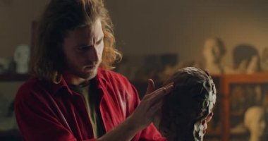 Lviv, Ukrayna - 12 Şubat 2020: Heykeltıraş çömlekçilikten insan kafası üzerinde çalışıyor. Milenyum adamı sanatçı atölyesinde ayakta duruyor ve heykel yapıyor. El yapımı sanat ve yaratıcılık kavramı.