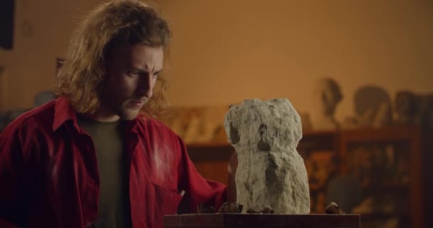 Lviv, Ukraine - 12 février 2020 : Homme travaillant avec un marteau et un ciseau plat tout en coupant une statue dans un bloc brut de gypse. Sculpteur tournant sculpter et souffler la poussière dans l'atelier d'art de la sculpture. — Video