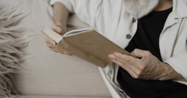 Crop view of male pensioner reading and spending free time. Homem velho barbudo desfrutando de livro enquanto sentado no sofá. Conceito de aposentadoria, lazer e tempo livre. — Vídeo de Stock