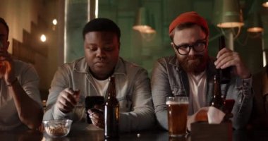 Zeki telefonlar kullanan ve barda yan yana otururken ekrana bakan genç insanlar. Çok ırklı bir grup insan telefon çalıyor ve bira içiyor. Bağımlılık kavramı.