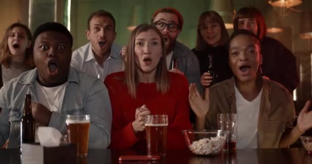 Joyeuses personnes diverses célébrant et souriant tout en regardant le jeu de sport. De jeunes amis heureux se réjouissent et crient tout en soutenant leur équipe préférée et en buvant de la bière au pub. — Video