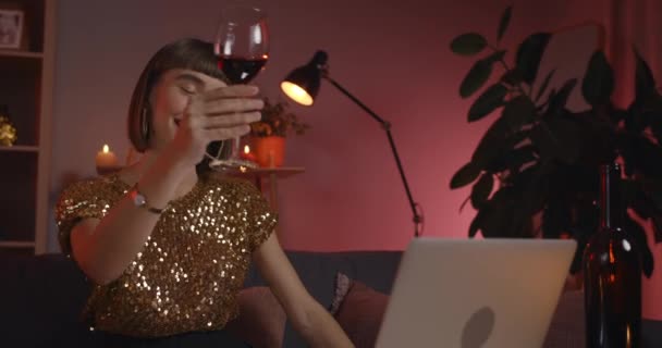 Primer plano de la mujer milenaria animando a la pantalla del ordenador portátil con vidrio y beber vino mientras habla. Persona femenina atractiva con anillo en la nariz sonriendo mientras recibe videollamadas en casa. — Vídeos de Stock