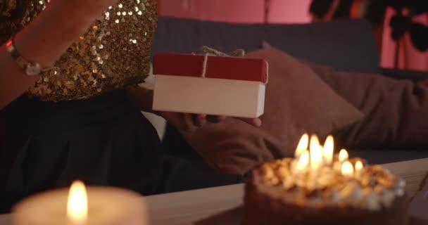 Crop view of woman holding present box on her knees. Cake with candles near her. Concept of birthday party. — Stock Video