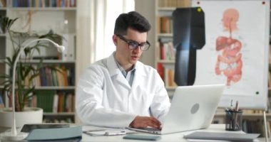 Beyaz elbiseli genç adam dizüstü bilgisayarda yazarken tıbbi form dolduruyor. Gözlüklü bir erkek doktor kişisel bilgisayarla çalışırken bilgi yazıyor. Çalışma ve rutin kavramı.