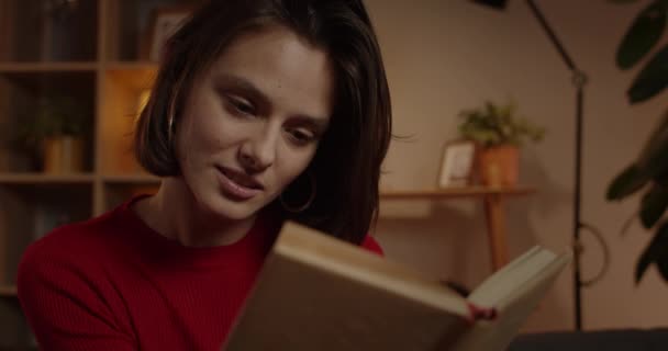 Närbild av brunett hår kvinnlig person läsa och spendera fritid. Attraktiv tusenårig kvinna njuter av boken medan du sitter på soffan i mysigt hem. Begreppet fritid. — Stockvideo