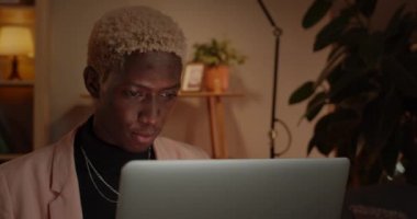Sofya 'da oturup dizüstü bilgisayar kullanan yakışıklı bir adamın yakın görüntüsü. Evde boyalı saçlı, internette gezinen konsantre Afro-Amerikan genç adam. Boş zaman kavramı..