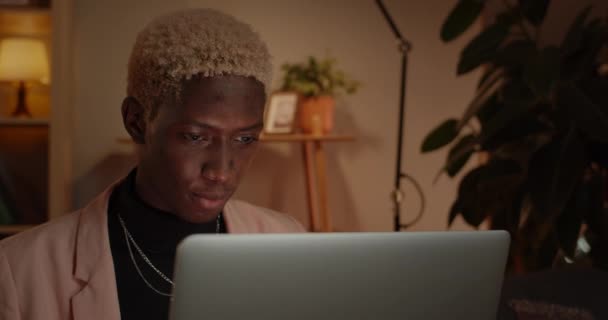 Close up view of beautiful man typing and using laptop while sitting on Sofa.Συγκεντρωμένος αφρο-αμερικανός νεαρός με βαμμένα μαλλιά περιηγείται στο διαδίκτυο στο σπίτι. Έννοια του ελεύθερου χρόνου. — Αρχείο Βίντεο