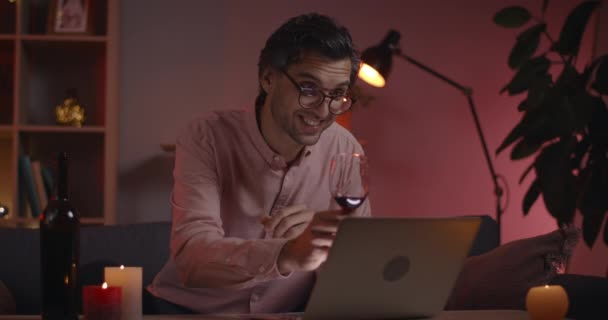Gözlüklü, şarap kadehiyle dizüstü bilgisayara tezahürat yapan ve konuşan erkek görüntüsü. Sohbet ederken gülümseyen, beyaz gömlekli neşeli bir adam. Çevrimiçi iletişim kavramı. — Stok video