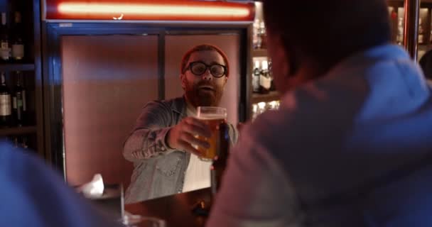Amical barman barbu servant verre de bière au client assis au comptoir. Concept de loisir. — Video