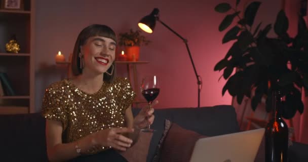 Crop view of attractive woman cheering to laptop screen with glass and drinking wine while talking. Beautiful female person smiling while having video call. Concept of online communication. — Stock Video