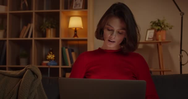 Crop view of attractive woman using laptop and smiling while sitting on sofa at home. Positive female person chatting with friends online. Concept of leisure and free time. — Stock Video