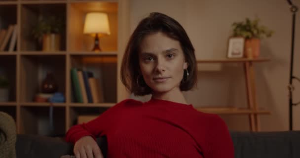 Vista de colheita de alegre jovem olhando para a câmera. Retrato de mulher milenar com cabelo morena curta posando enquanto sentado em casa à noite. Ampliar. — Vídeo de Stock