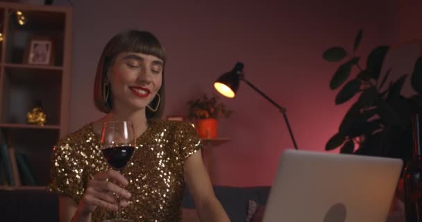 와인 잔을 들고 노트북 화면을 보면서 이야기하는 젊은 여성의 모습. 환하게 웃으며 떠들고 있는 쾌활 한 여자. 온라인 대화의 개념. — 비디오