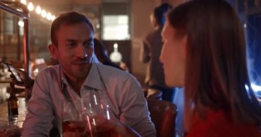 Barda oturup gülümseyen neşeli kadın ve adamın yakın görüntüsü. Mutlu çift, akşam birlikte vakit geçirirken barda iletişim kuruyor ve bira içiyor..