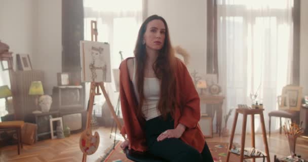 우크라 이나 리비우: 2020 년 1 월 17 일: 여성 이 고개를 돌려 카메라를 본다. 창조 스튜디오에서 의자에 앉아 있는 동안긴 머리를 하고 있는 브루 네트 여성 화가의 초상화. 집안으로. — 비디오
