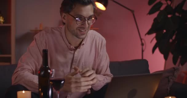 Hombre guapo saludando y hablando mientras tiene conversación en línea. Persona masculina positiva en gafas sonriendo mientras mira a la pantalla del ordenador portátil en casa. Concepto de fecha en línea. — Vídeos de Stock